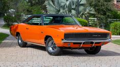 an orange muscle car parked in front of a house