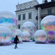 a person walking in front of giant bubbles on the ground outside an apartment building with snow