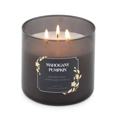 a candle with three candles in it on top of a white surface and the words mahogany pumpkin