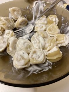 a bowl filled with dumplings covered in white sauce and a fork sticking out of it