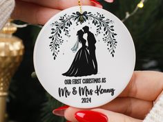 a hand holding a christmas ornament with a bride and groom kissing on it