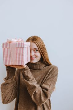 a woman is holding up a pink gift box