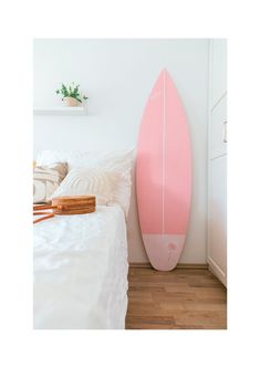 a pink surfboard sitting on top of a bed next to a white wall and wooden floor