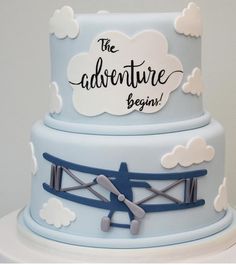 a blue and white cake with an airplane on it's side that says the adventure begins