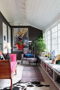 a living room filled with lots of furniture next to a window covered in plants and potted plants