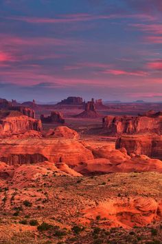 the desert is full of red rocks and green plants at sunset with pink clouds in the sky