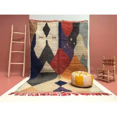 a chair and rug on the floor in front of a pink wall with a ladder