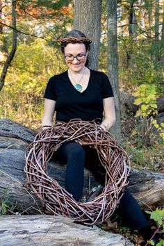 a woman sitting on top of a tree stump holding a wreath made out of branches