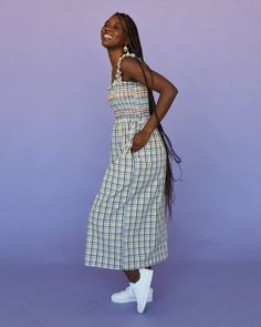 a woman standing in front of a purple background wearing a plaid dress and white tennis shoes