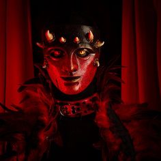 a man with red and black makeup is in front of a red curtain while wearing horns on his head