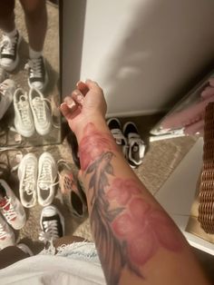 a person with a tattoo on their arm sitting in front of several pairs of shoes