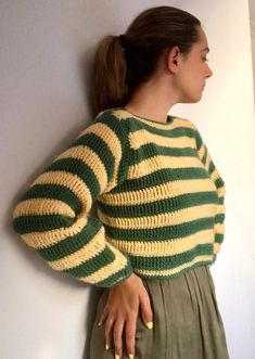 a woman standing against a wall with her hand on her hip wearing a green and yellow striped sweater