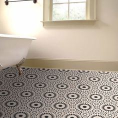 a bath tub sitting under a window next to a white sink in a bathroom with black and white tile on the floor