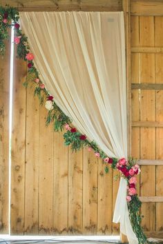 an image of flowers on the side of a wooden wall with white drapes and greenery