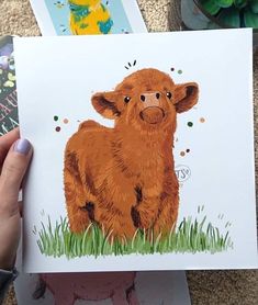 a person holding up a card with an image of a brown cow in the grass