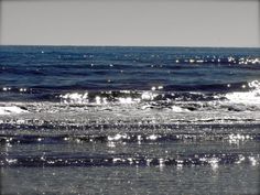 an ocean view with the sun shining on the water and some waves coming in to shore