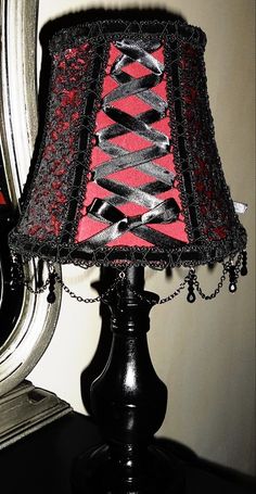 a lamp with a red and black shade on top of it next to a mirror