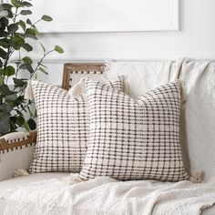 two pillows sitting on top of a white couch next to a potted green plant