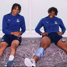 two young men sitting on top of a bed next to each other wearing blue shirts