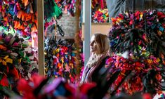 a woman standing in front of a large display of colorful wreaths and streamers