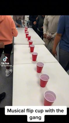 red cups lined up on top of a long table with people standing around and looking at them