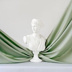 a white busturine sitting on top of a table next to a green curtain