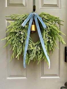 a green wreath with blue ribbon hanging on the front door and a bell in the middle