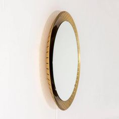 a round mirror mounted to the side of a white wall next to a wooden shelf