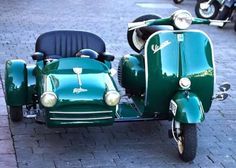 an old green motorcycle with sidecar parked on the street next to other motor scooters