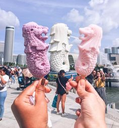 two people holding up candy pops in front of a fountain with buildings in the background