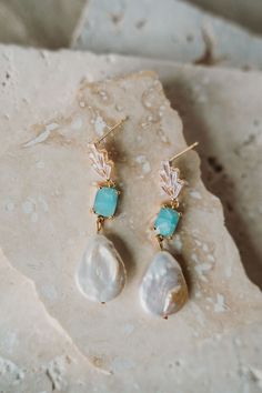 a pair of earrings with pearls and turquoise stones on top of a stone slab next to a rock