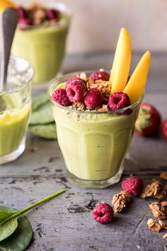 two glasses filled with green smoothie and topped with raspberries, oats, and nuts