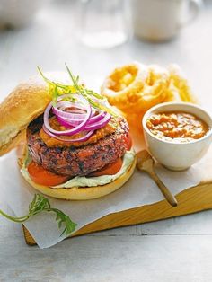 a burger with onion, lettuce and tomato on a wooden tray next to some fries