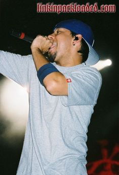 a man singing into a microphone while wearing a blue hat and grey shirt with red lettering on it