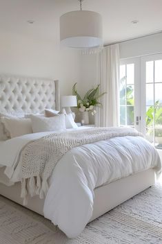 a white bed sitting in a bedroom next to a window covered in curtains and pillows