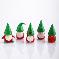 small plastic christmas gnomes are lined up on a white surface with one wearing a green hat and the other red