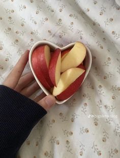 someone is holding an apple in a heart shaped bowl