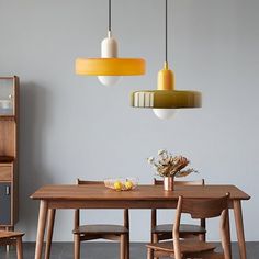 a dining room table and chairs with yellow pendant lights above it, in front of a gray wall