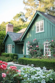 a green house with roses growing on the windows and bushes around it's perimeter