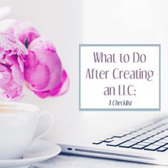 a cup of coffee sitting next to a laptop computer on a desk with pink flowers in front of it