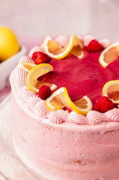 a pink cake with lemons and raspberries on top is sitting on a plate