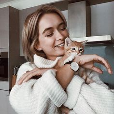 a woman holding a kitten in her arms while wearing a white sweater and looking at the camera