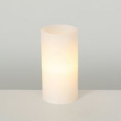 a white candle sitting on top of a table next to a gray wall and floor