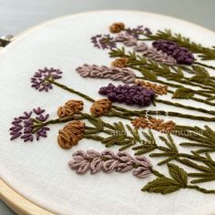 a close up of a embroidery on a white cloth with purple and green flowers in it