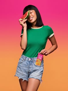 a woman holding a slice of watermelon in front of her face and smiling