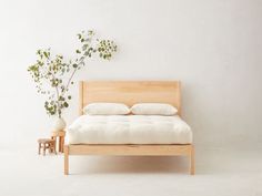 a bed with white sheets and pillows next to a plant on the side of it