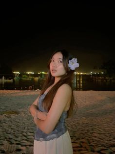 a woman standing on the beach at night with her arms crossed and flowers in her hair