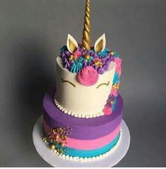 a three tiered cake decorated with flowers and a unicorn's horn