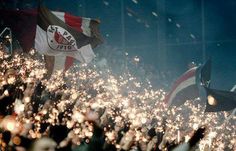 many people are holding flags and waving in the air at an outdoor event with bright lights shining on them