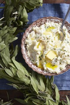 a bowl filled with mashed potatoes and herbs on top of a blue cloth next to green leaves